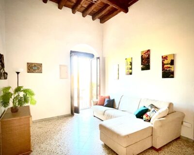 Soggiorno con divano ad angolo, piante e accesso al balcone nell'appartamento Comandante del Borgo.